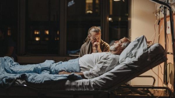 A man dying in a hospital as a woman holds his hand