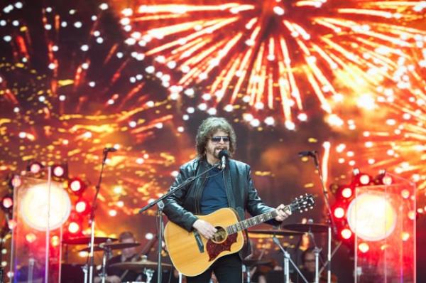 Jeff Lynne plays guitar on stage at Glasto<em></em>nbury festival. Fireworks are displayed behind him.