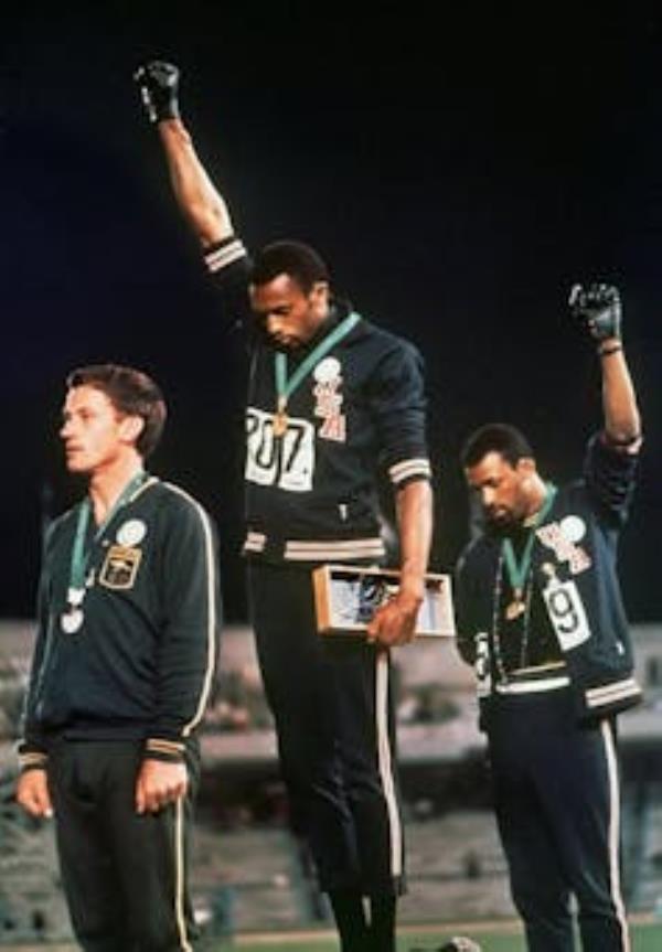 Two athletes with fists raised in protest standing on Olympic podium.