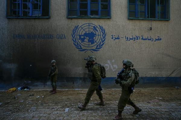 Soldiers in fatigues and helmets walk past a building with a UN logo on it.