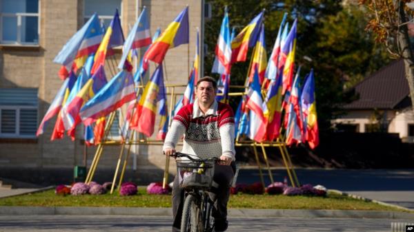 A man cycles backdropped by Moldovan and Gagauz flags in Comrat, the capital of Gagauzia, an auto<em></em>nomous part of Moldova, Nov. 2, 2024, ahead of a presidential election runoff taking place Nov. 3. 