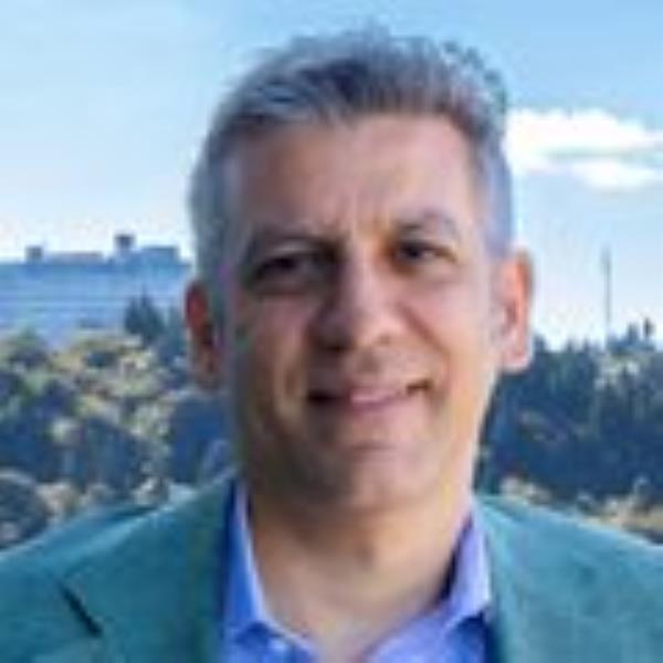 Steven Mansoor, M.D., Ph.D. stands atop the Center for Health and Healing building with the OHSU tram and Marquam hill viewable in the distance.